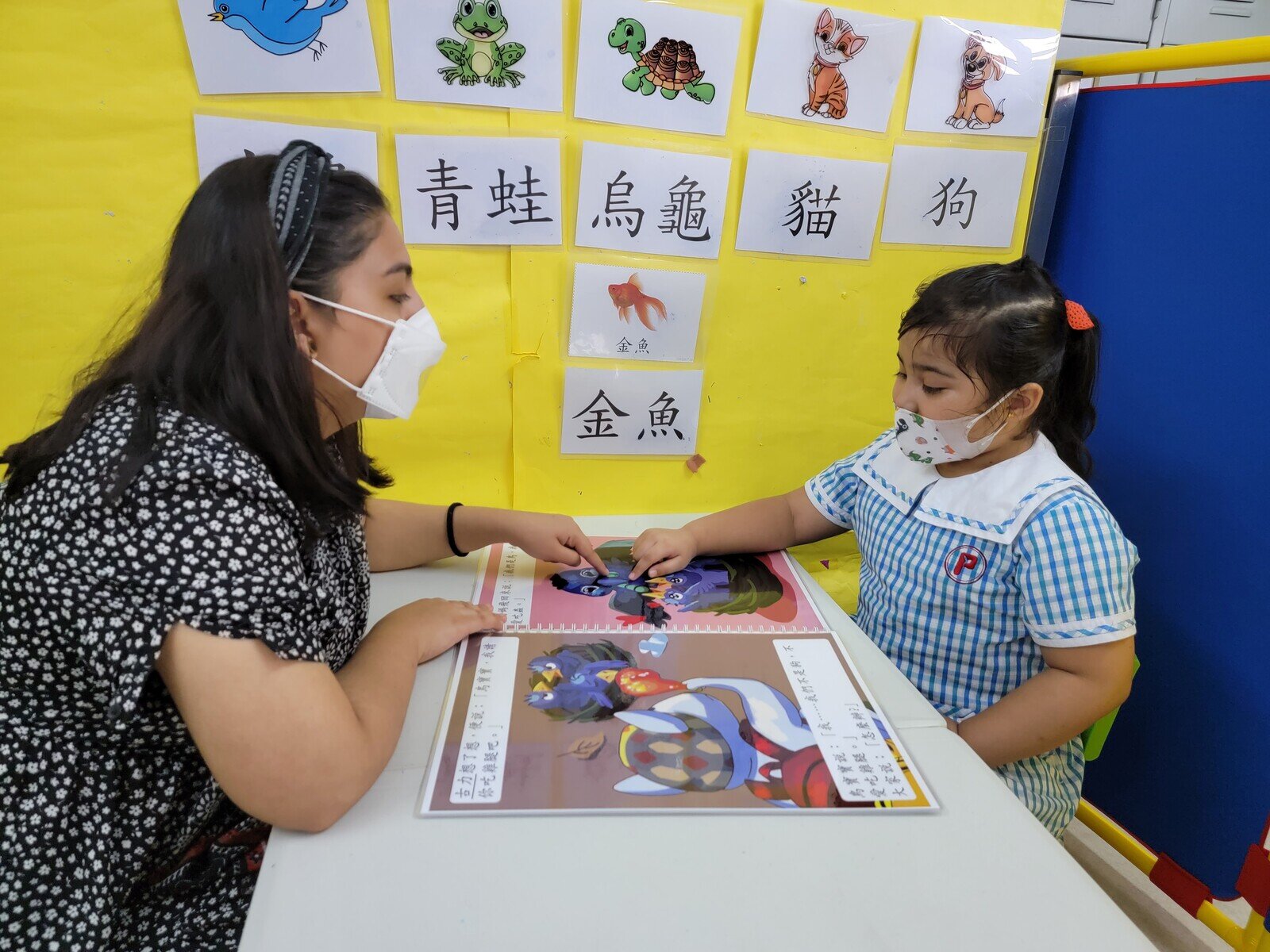 Soha reading a designated picture book that is part of the scheme with the help of her teacher. 