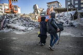 两名当地居民从他们被毁坏的房屋中收拾物品，然后加入了数千名流离失所的灾难幸存者的行列。